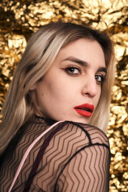 Altın bir arka planda ceketle poz veren şık bir kız..