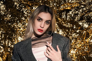 Altın bir arka planda ceketle poz veren şık bir kız..