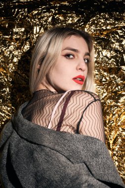 Altın bir arka planda ceketle poz veren şık bir kız..