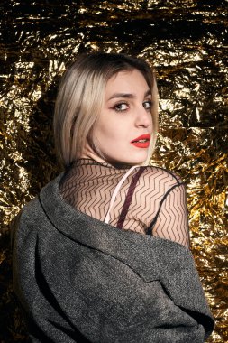 Altın bir arka planda ceketle poz veren şık bir kız..