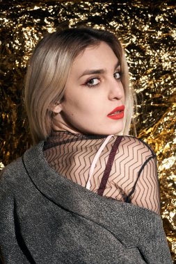 Altın bir arka planda ceketle poz veren şık bir kız..