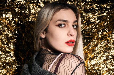 Altın bir arka planda ceketle poz veren şık bir kız..