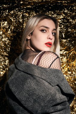 Altın bir arka planda ceketle poz veren şık bir kız..