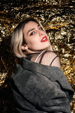 Altın bir arka planda ceketle poz veren şık bir kız..