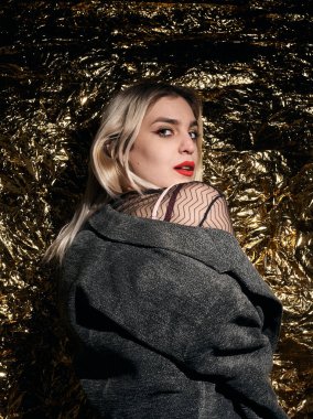 Altın bir arka planda ceketle poz veren şık bir kız..