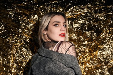 Altın bir arka planda ceketle poz veren şık bir kız..