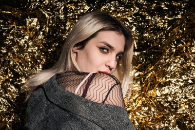 Altın bir arka planda ceketle poz veren şık bir kız..