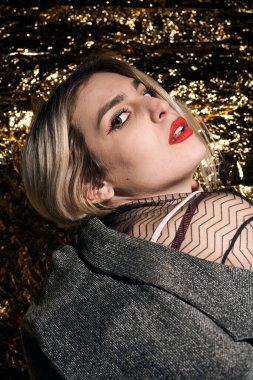 Altın bir arka planda ceketle poz veren şık bir kız..