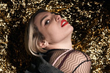 Altın bir arka planda ceketle poz veren şık bir kız..