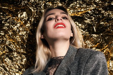 Altın bir arka planda ceketle poz veren şık bir kız..