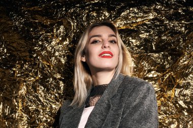 Altın bir arka planda ceketle poz veren şık bir kız..