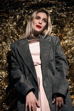 Altın bir arka planda ceketle poz veren şık bir kız..