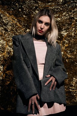 Altın bir arka planda ceketle poz veren şık bir kız..