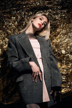 Altın bir arka planda ceketle poz veren şık bir kız..