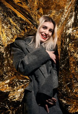 Altın bir arka planda ceketle poz veren şık bir kız..