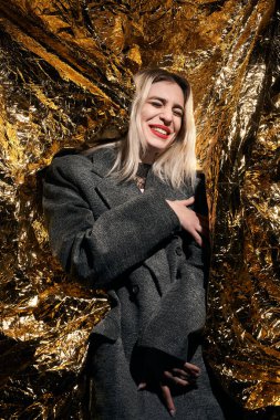 Altın bir arka planda ceketle poz veren şık bir kız..