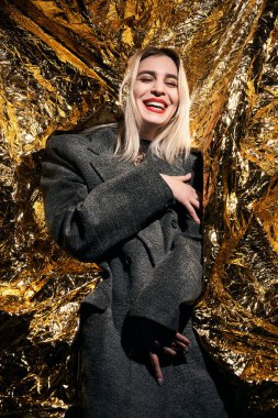 Altın bir arka planda ceketle poz veren şık bir kız..