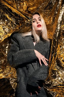 Altın bir arka planda ceketle poz veren şık bir kız..