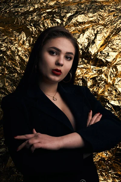 Stylish chubby girl posing in a black jacket on a gold background.