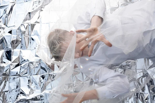 Yakışıklı bir manken gümüş folyoda tül kumaşın altında yatıyor..