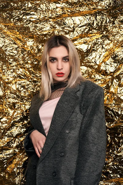Altın bir arka planda ceketle poz veren şık bir kız..