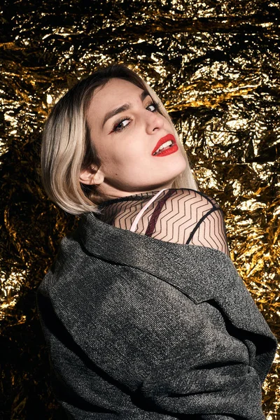 Altın bir arka planda ceketle poz veren şık bir kız..