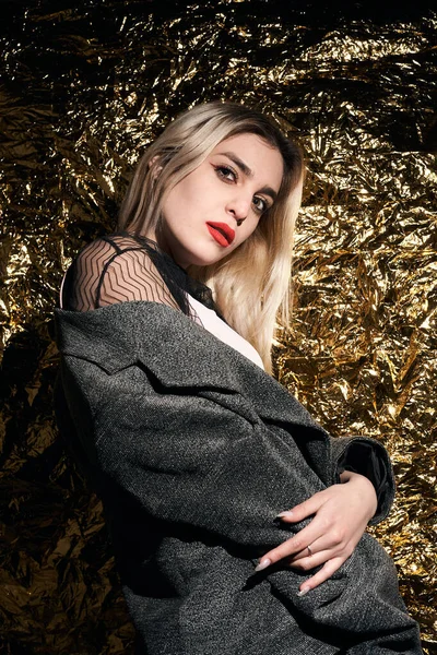 Altın bir arka planda ceketle poz veren şık bir kız..