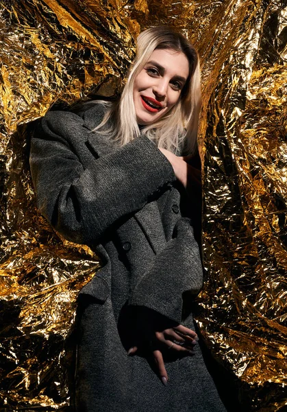 Altın bir arka planda ceketle poz veren şık bir kız..