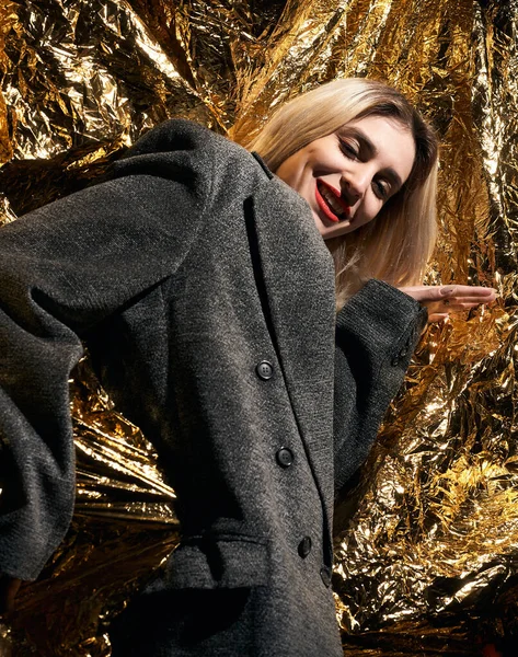 Altın bir arka planda ceketle poz veren şık bir kız..