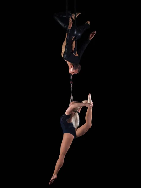 Two acrobats perform a dangerous stunt on hanging ropes in the air. A man holds a girl in his teeth. Isolated on a black background.