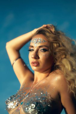 Yapışkan yapay elmaslar ve parıltılardan vücudun ve yüzün sanat yapısı. Peri perisi doğada, taşların ve suyun yanında yaşar. Fotoğrafın yumuşatma etkisi var, bir fikir olarak yapılmış..