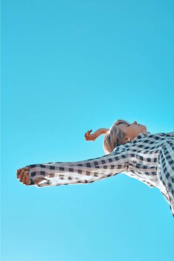 Mavi gökyüzüne karşı poz veren ekose elbiseli hoş, şık bir kız..