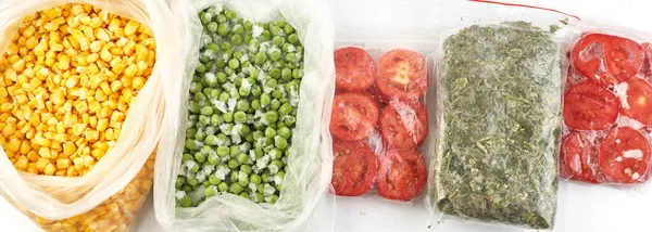 Set of frozen food packed in bags. Store vegetables for the winter, top view. Tomato, green peas, corn, greens.