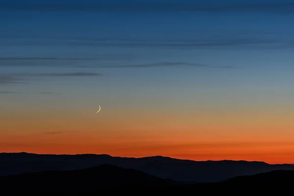 狭い三日月とダークブルーの空オレンジ色の夕日の背景に山の上で雲の美しい夜の風景 — ストック写真