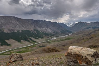 Dolambaçlı bir nehir, Vadisi, karlı dağlar tepeler ve bulutlu bir gökyüzü arka planı yamaçlarında yeşil orman manzaralı üstten görünüm