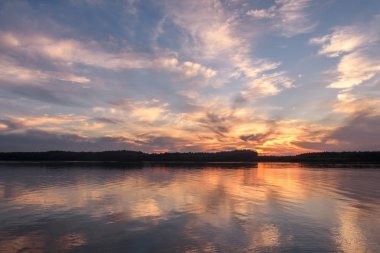 Amazing sunset on the river with beautiful clouds in the sky, trees, reflections in the water, waves and ripples