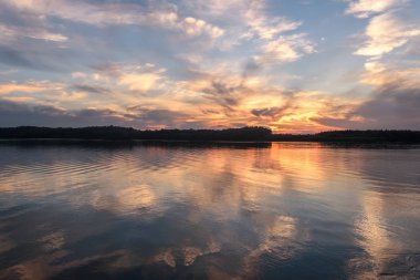 Amazing sunset on the river with beautiful clouds in the sky, trees, reflections in the water, waves and ripples