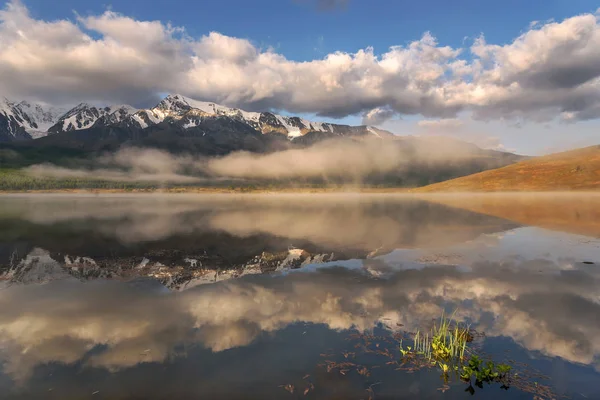 美妙的镜子反射美丽的云彩 山被雪和森林覆盖 并且薄雾在湖的光滑的水在黎明 — 图库照片