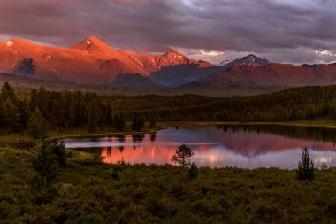 Güzel bir göle, dağlar, orman ve ağaç bulutlar yağmur sonra ile fırtınalı gökyüzü karşı üzerinde şaşırtıcı kırmızı günbatımı
