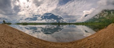 Adam güzel kabarık bulutlar, yeşil ağaçlar, dağlar, sis ve göle ayna yansımaları ile şaşırtıcı panorama hayran