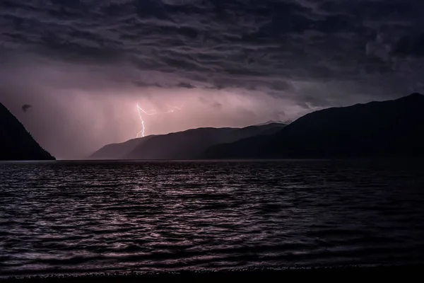 Lightning in dark blue clouds during a thunderstorm over a lake in the mountains