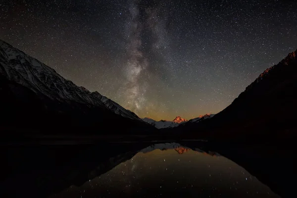 雪の山 月の出と湖の反射からバックライト付きの山の峰の上の天の川銀河と夜の星空の驚くべきパノラマ — ストック写真