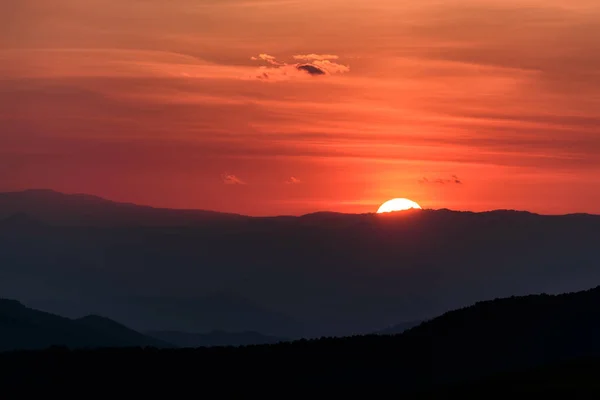 山の輪郭に太陽の円板と空に照らされた雲との驚くべき燃えるような夕日 — ストック写真