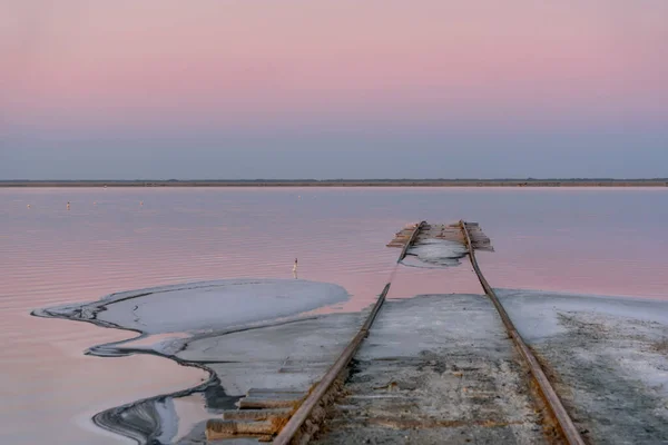 Tuz gölü üzerinde pembe bir gün doğumu, kıyıya giden raylar ve ön plandaki tuz. Bursol Gölü, Altai, Rusya.