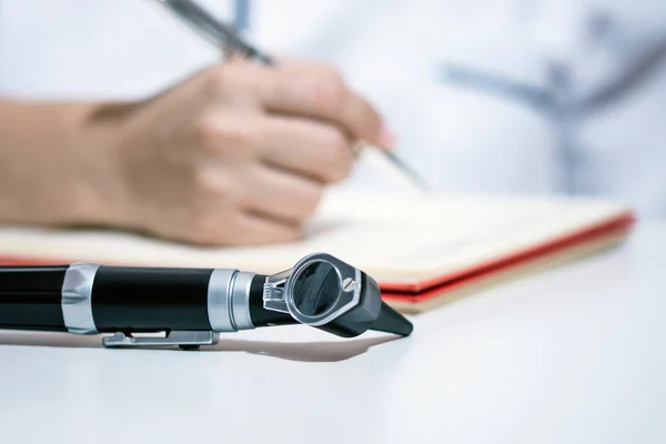 Doctor desk with otoscope, doctor hand with pen writing on clipboard