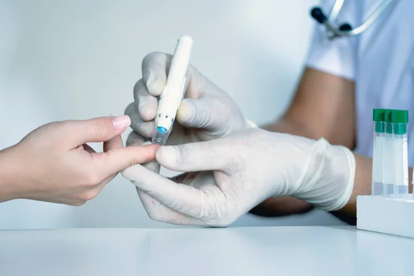 Doctor checking blood sugar level, doctor using lancelet on finger, testing blood glucose