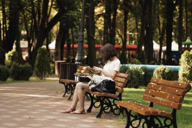 Elinde telefon ile parkta bir bankta oturan gitar ile genç kadın