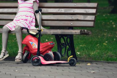 Scooter ile parkta bir bankta oturan çocuk 
