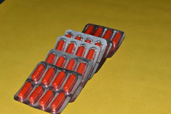 Cápsulas de píldora roja en blister aisladas sobre fondo amarillo, en las tiras . —  Fotos de Stock