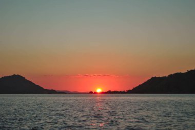Deniz yüzeyinin altında büyük sarı güneş ile parlak gün batımı. Tropik Komodo adasında Güzel Gün Batımı, Labuan Bajo, Fores, Endonezya